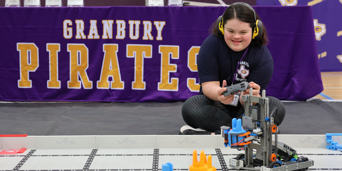 Participant operates a VEX IQ Robotics Competition robot on a practice field